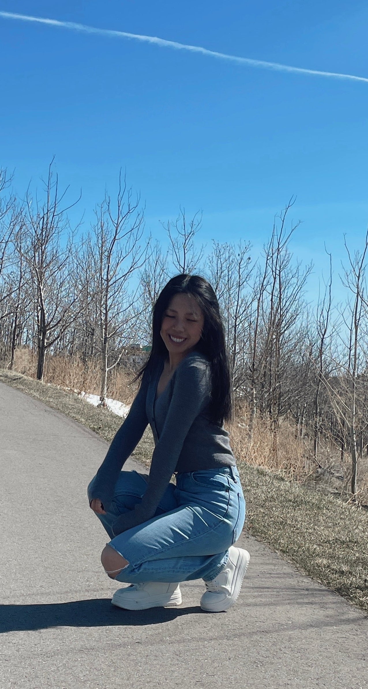 Person in a blue outfit crouching on a road with a clear blue sky.